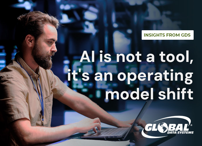 IT professional working on a laptop in a network operations center with the headline “AI is not a tool, it’s an operating model shift.”